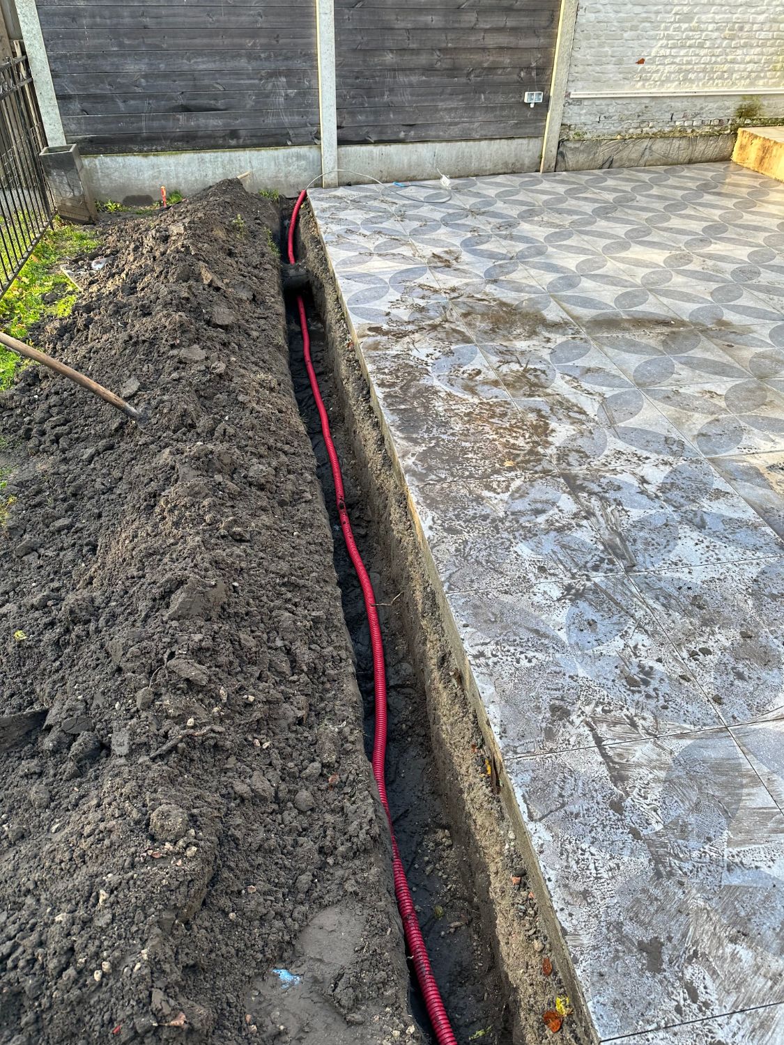 Om een veilige en duurzame installatie te garanderen, is er een sleuf gegraven langs het terras. Hierin is een hoogwaardige rode mantelbuis geplaatst voor een optimale bescherming van het grondkabeltraject.