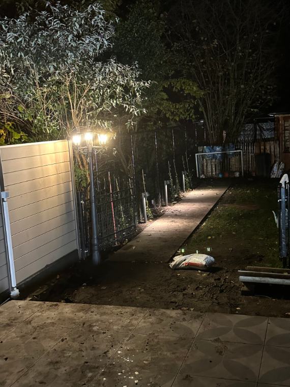 Een prachtig nachtbeeld van het eindresultaat. De klassieke lantaarnpaal vormt een stijlvol blikvanger, terwijl de staande armaturen het tuinpad doeltreffend en sfeervol uitlichten.